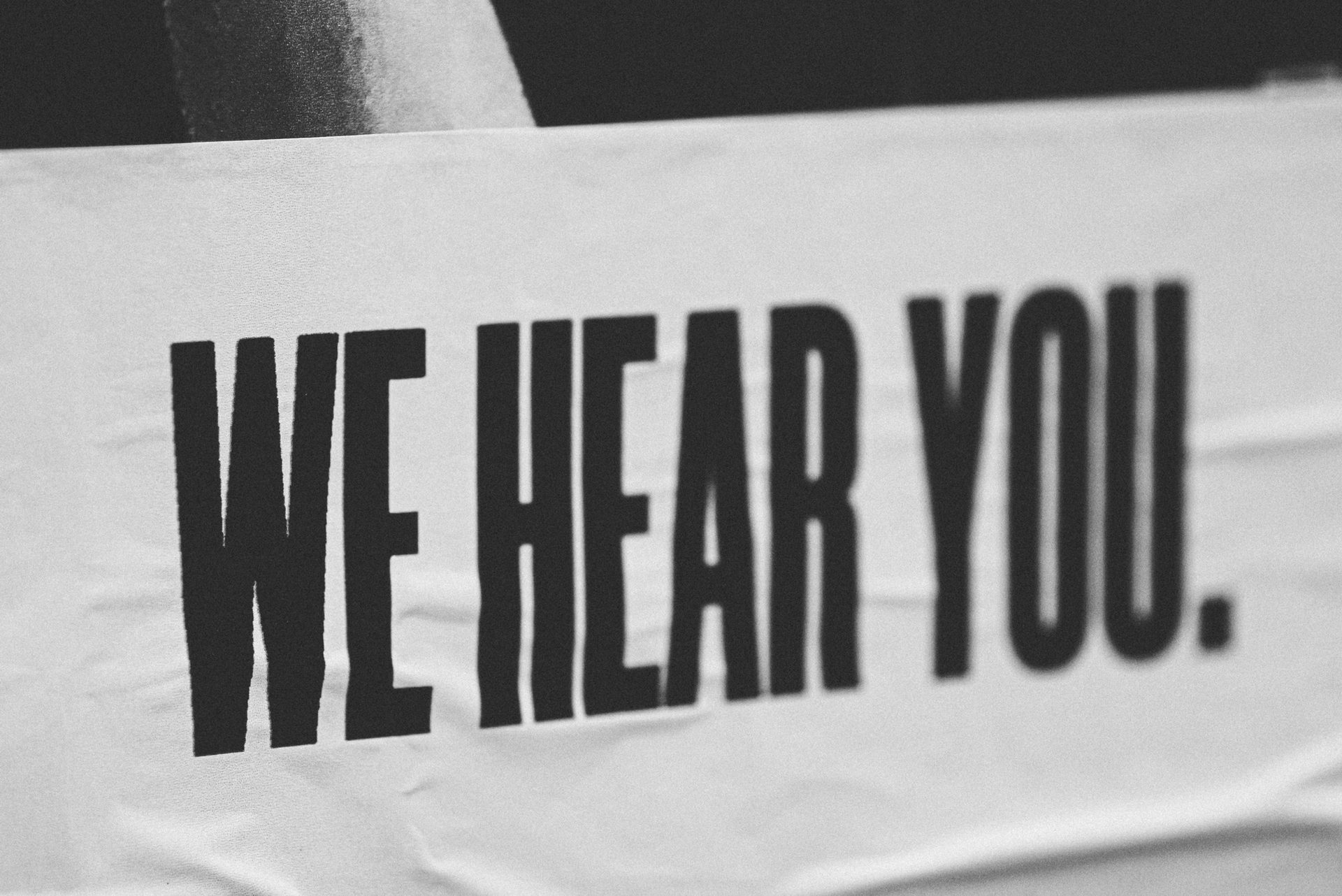 Black-and-white close-up of a poster that reads "WE HEAR YOU."